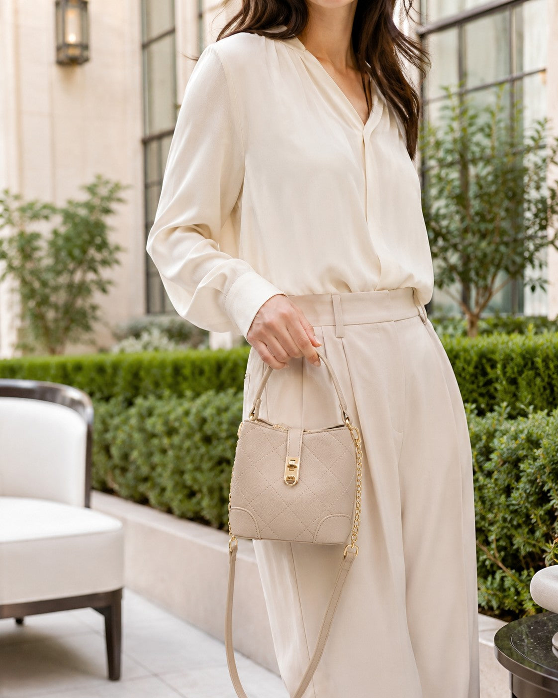 VALENORA Margot quilted beige vegan leather bucket shoulder bag with gold turn-lock and chain detail held by a model.