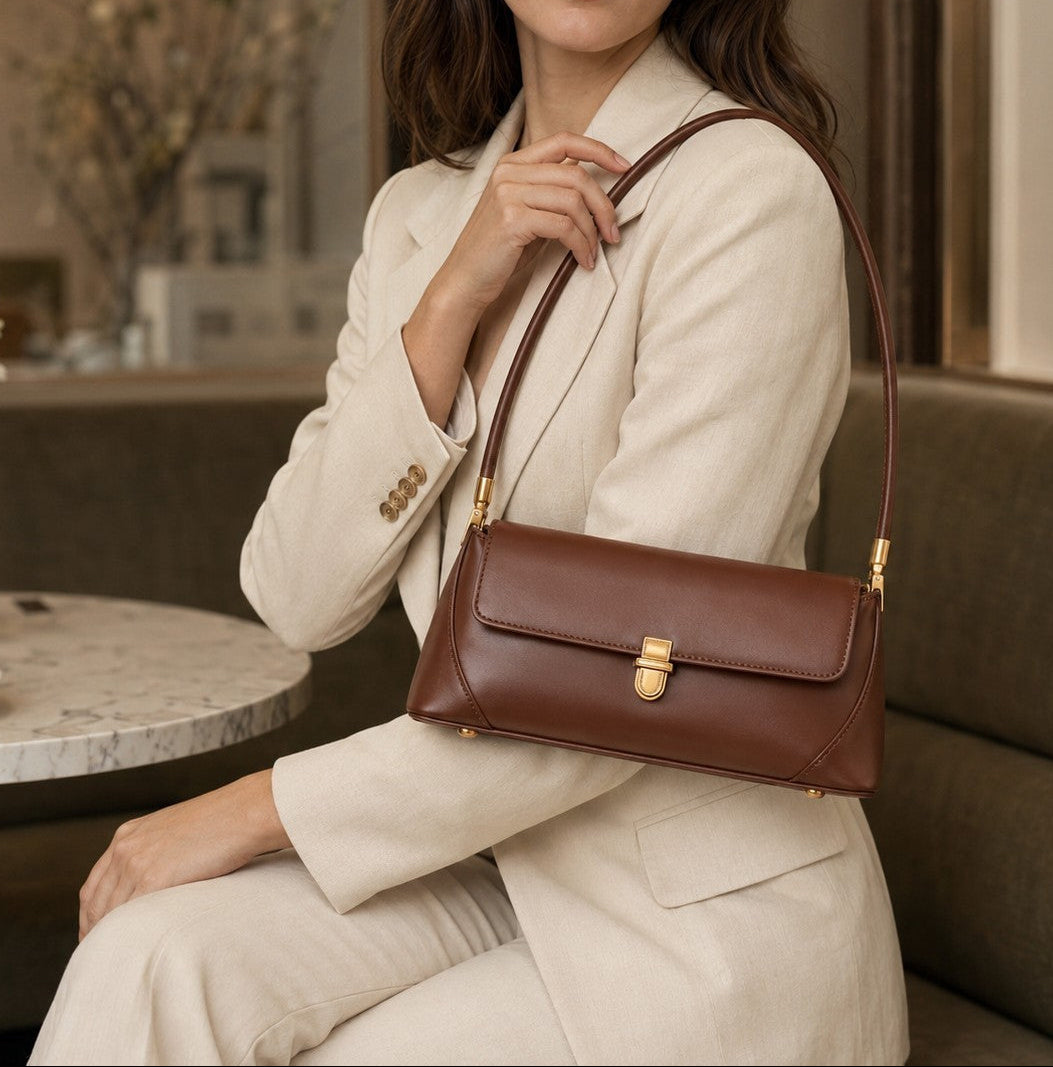 VALENORA Amancia brown synthetic leather baguette shoulder bag with gold hardware worn by a woman in a beige suit