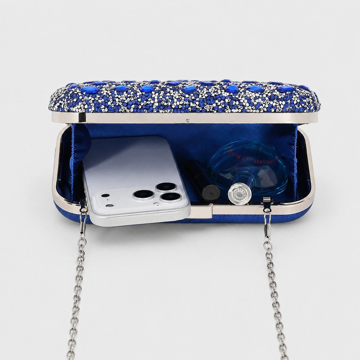 VALENORA cobalt blue crystal-embellished hard-shell clutch bag open with a smartphone and perfume bottle inside