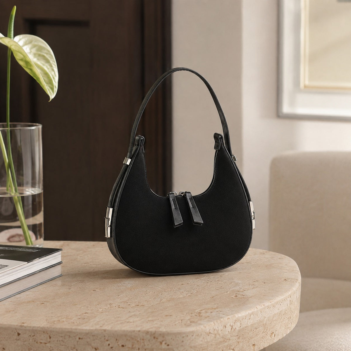VALENORA French black suede and leather shoulder bag with a rounded silhouette and silver hardware on a stone table.