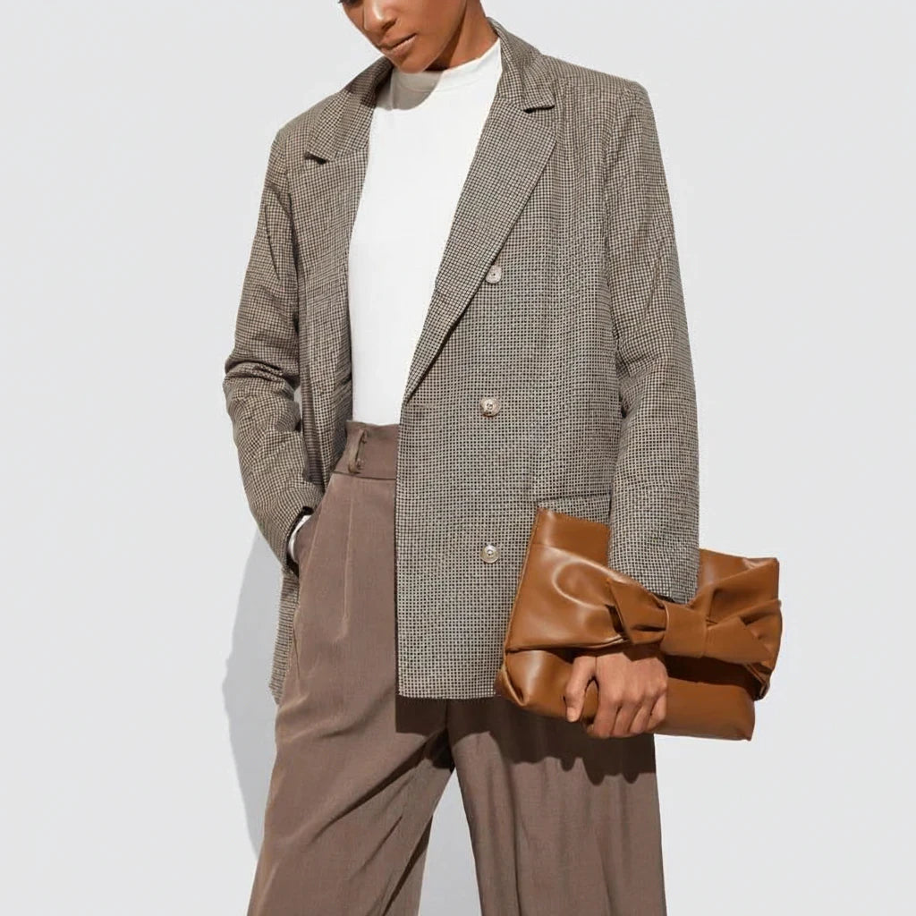 VALENORA brown leather handbag with a front bow detail held by a model in a blazer and trousers
