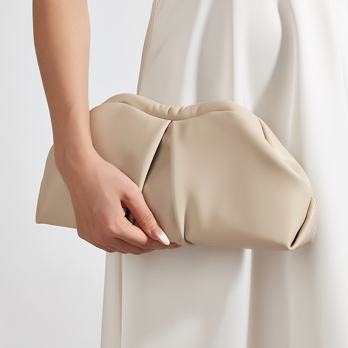 VALENORA Colette clutch bag in beige vegan leather with a soft pleated design held in hand against a white dress