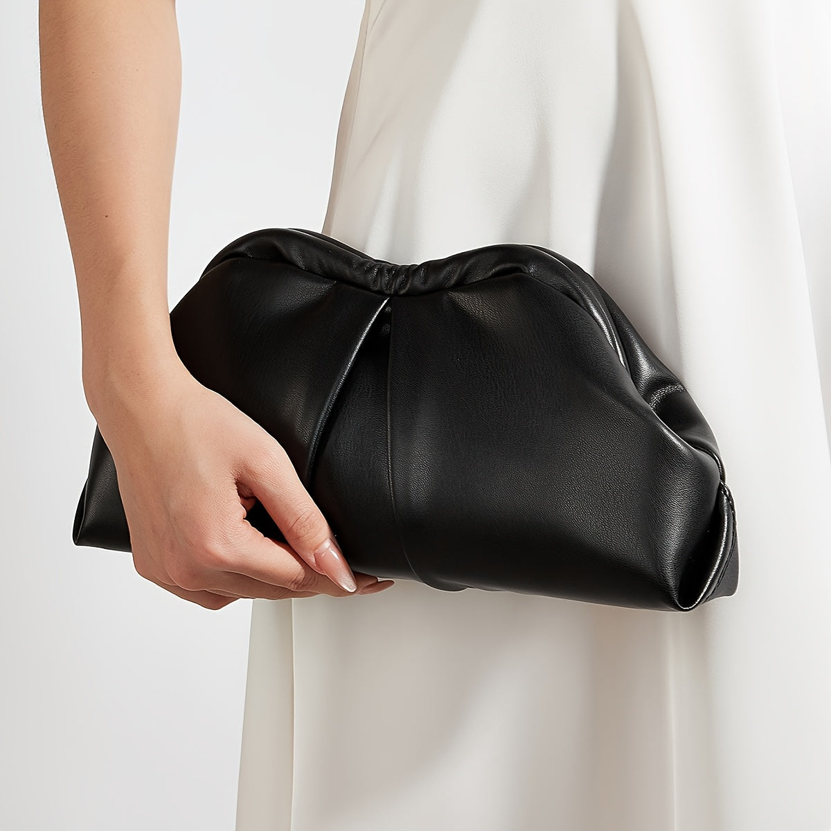 VALENORA Colette clutch bag in black vegan leather with a soft pleated design held by a woman in a white dress