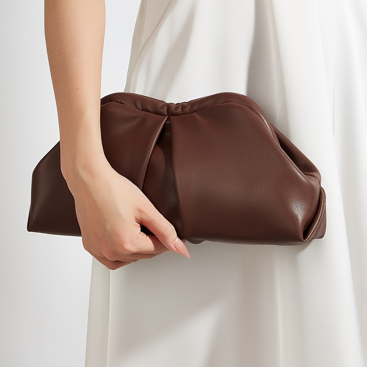 VALENORA Colette clutch bag in dark brown vegan leather with a soft pleated design held by a woman in a white dress.