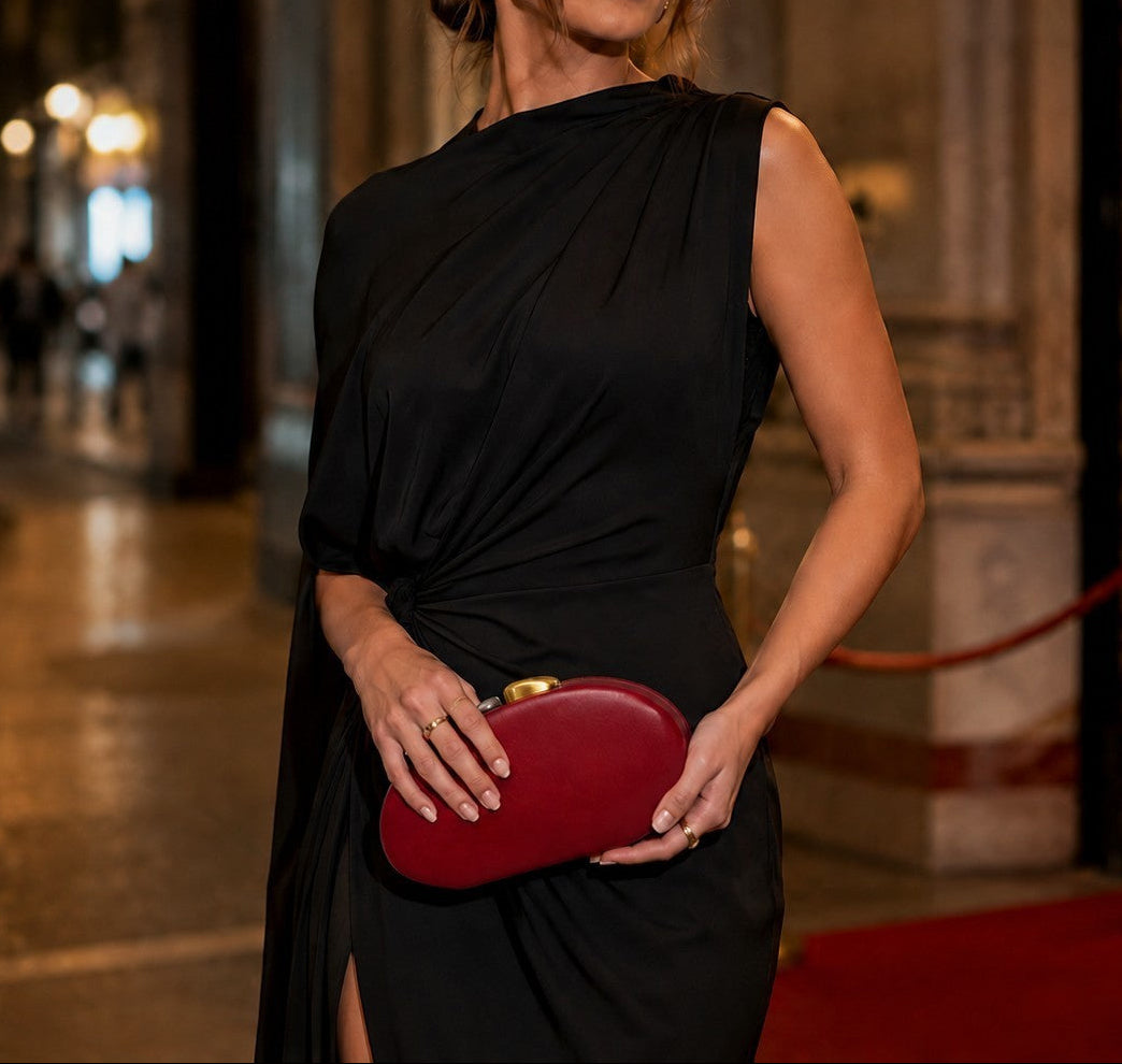 VALENORA Cosette clutch in red vegan leather with a two-tone gold and silver clasp held by a woman in a black dress.