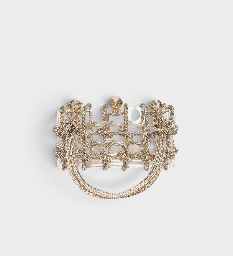 VALENORA Isabelle transparent acrylic clutch bag with a decorative gold knotted rope overlay and gold hardware.