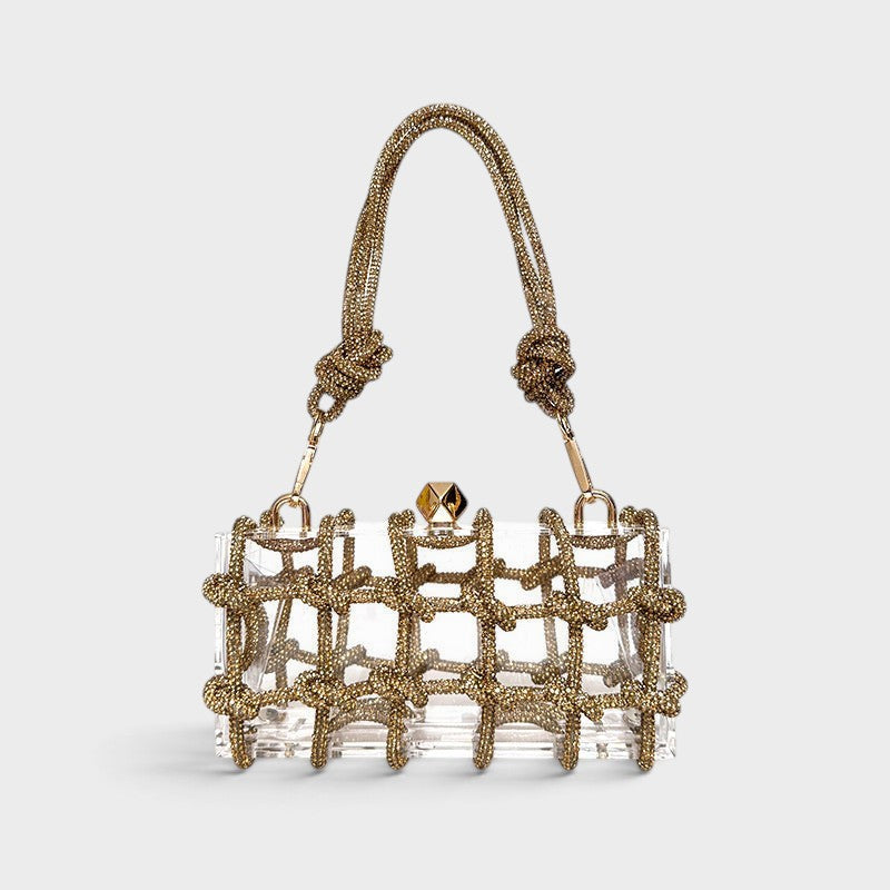 VALENORA Isabelle transparent acrylic clutch bag with a gold beaded grid overlay and matching gold knotted handle.