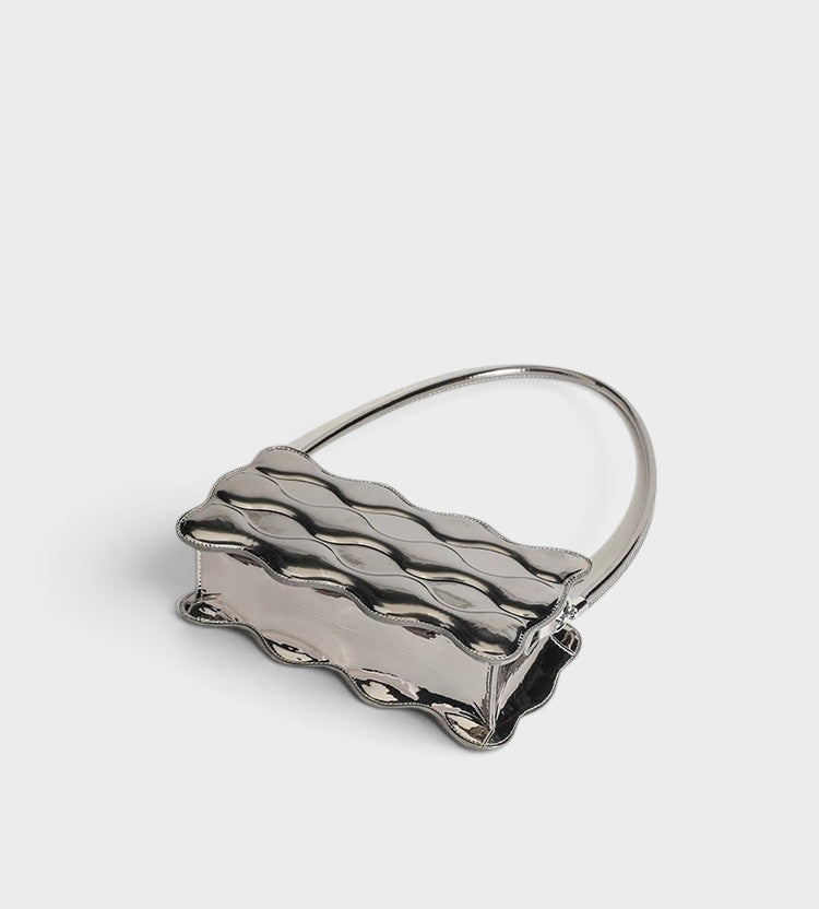VALENORA Luna Wave shoulder bag in metallic silver vegan leather with a unique sculptural curved silhouette.