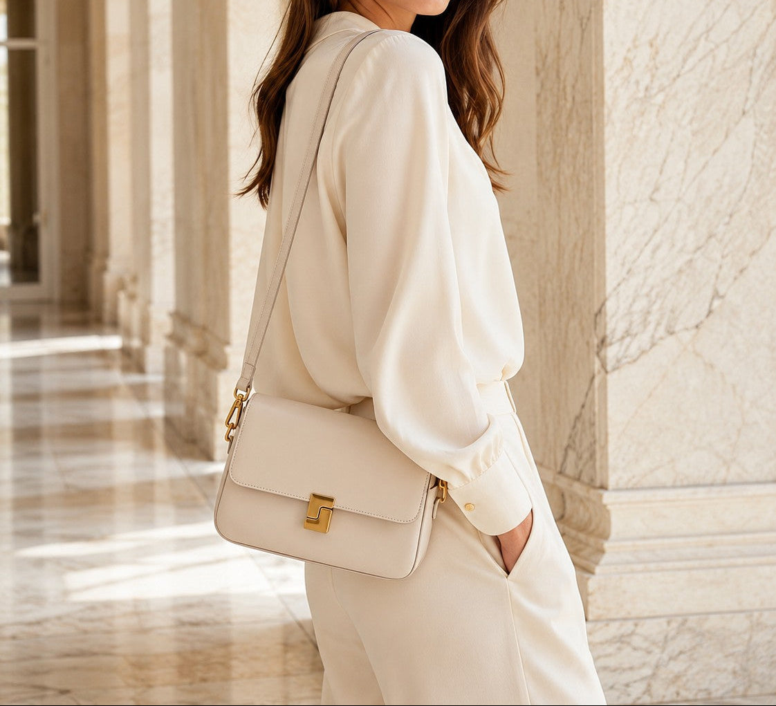 VALENORA Marisa shoulder bag in cream cowhide leather with a gold-tone buckle, worn by a woman in a matching outfit.