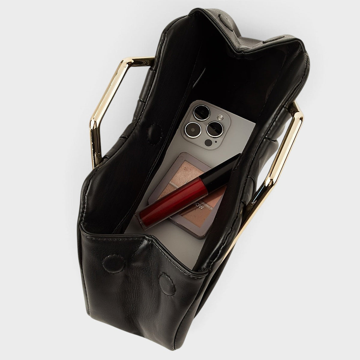 VALENORA Natalie black pleated vegan leather handbag with gold metal handles, shown from above with daily essentials.