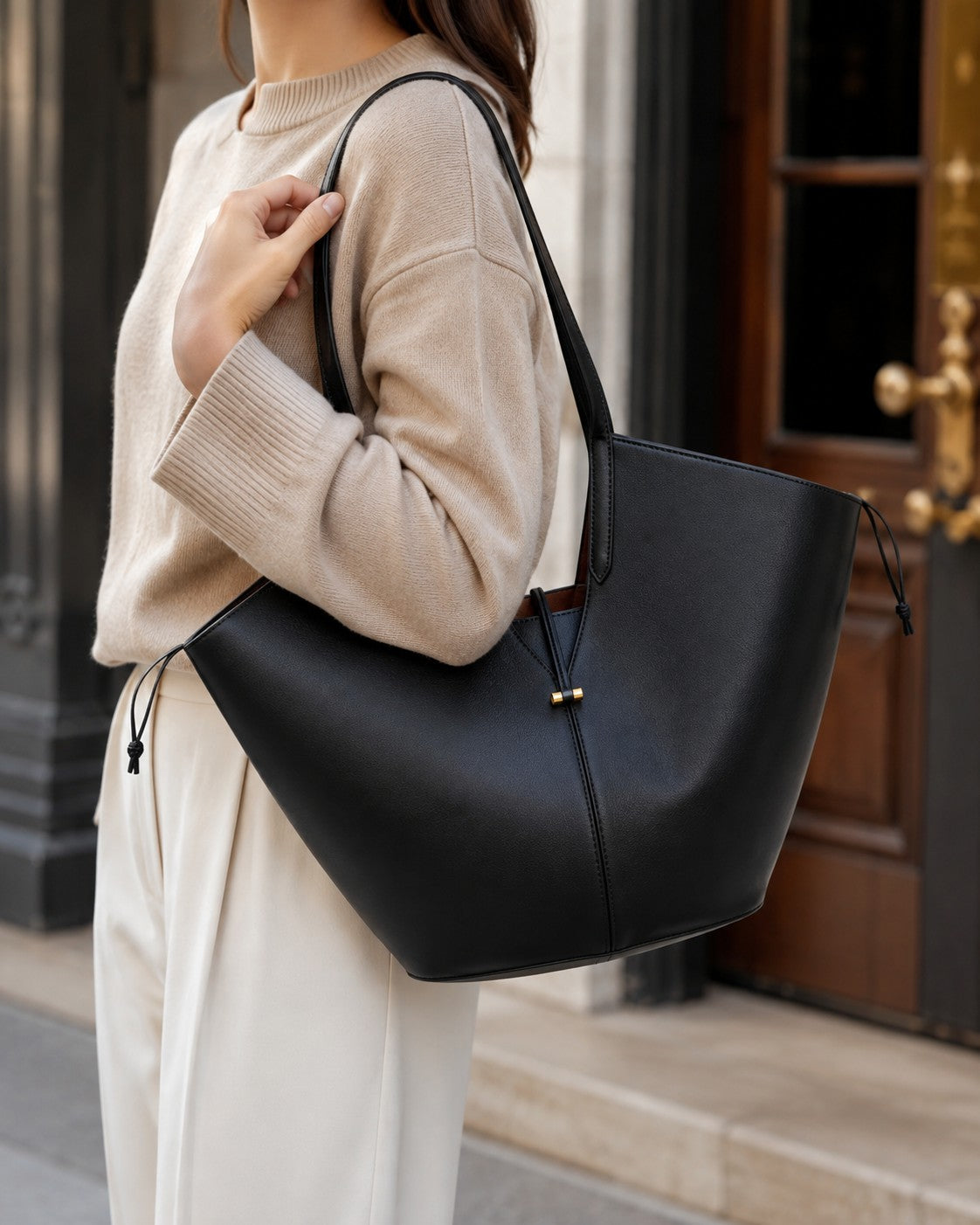 VALENORA Solene black vegan leather tote bag with a sculptural wraparound handle and gold toggle detail on shoulder.