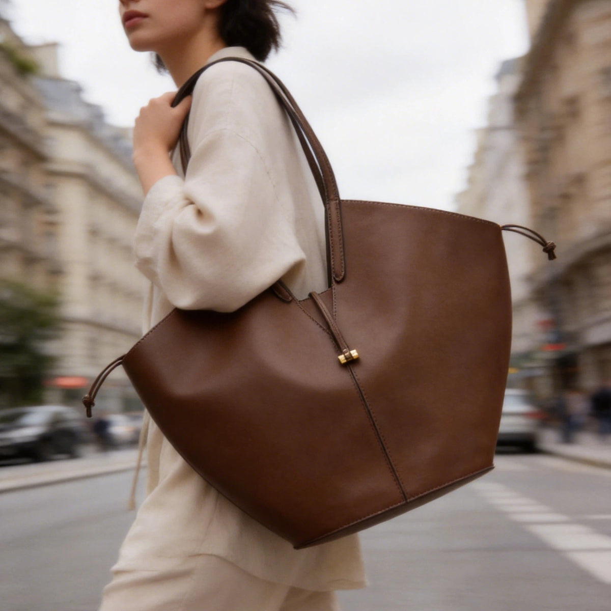 VALENORA Solene brown vegan leather tote bag with a sculptural wraparound handle and gold toggle detail on a city street