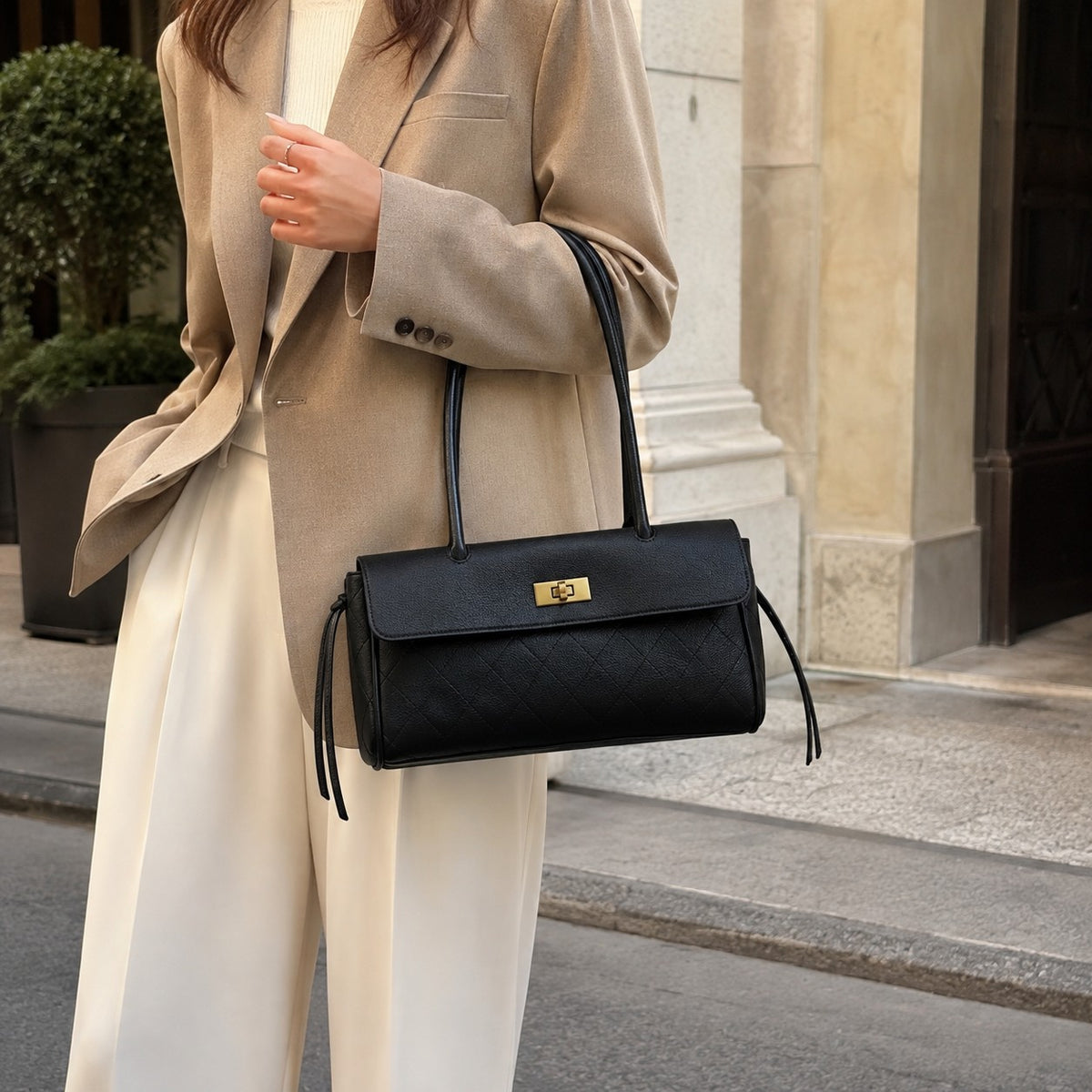 VALENORA Verancia black quilted shoulder bag with gold turn-lock closure and side-tie detail worn with a beige blazer.