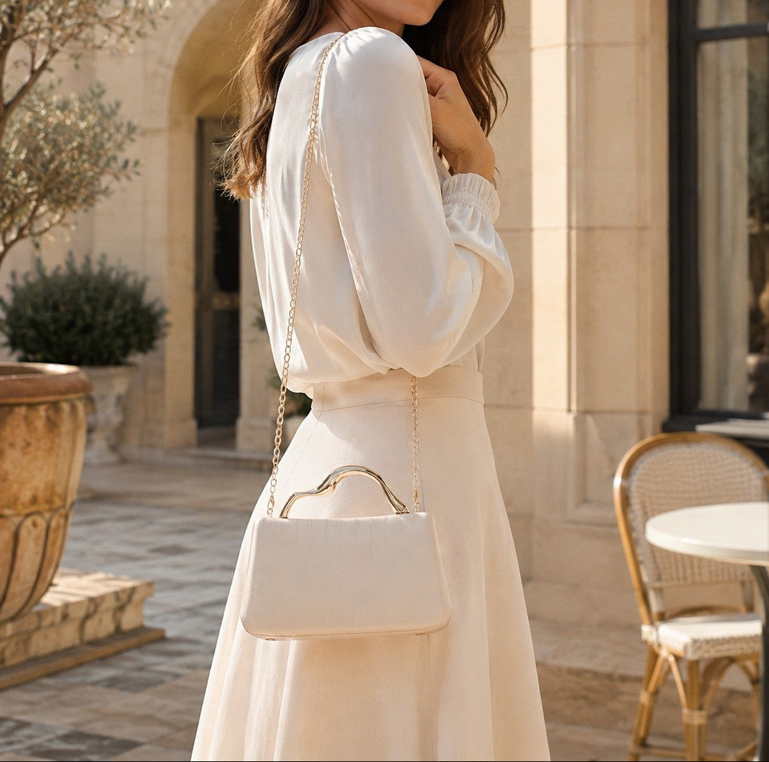 VALENORA Verena cream vegan leather clutch bag with a gold sculptural handle worn by a woman in a cream outfit